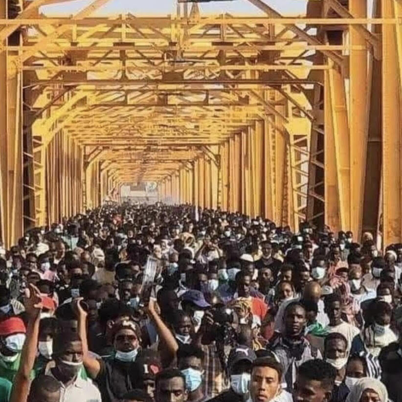 A bridge is swarmed with protestors, many masked and holding their arms up in emphasis